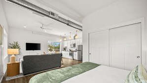 Un dormitorio moderno con una cama grande, un televisor y una kitchenette al fondo.