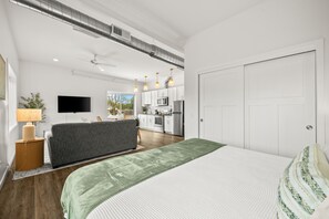 Ein modernes Schlafzimmer mit einem großen Bett, einem Fernseher und einer Küchenzeile im Hintergrund.