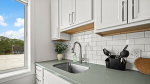 Una cocina con armarios blancos, un lavamanos de acero inoxidable, una planta en maceta y un bloque de cuchillos.