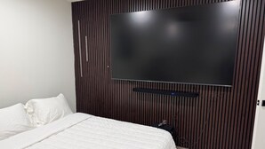 A bedroom with a large bed, a flat-screen TV mounted on a wooden panel wall, and a bedside table. - 3 Bedroom Home with Private Pool (Schertz)