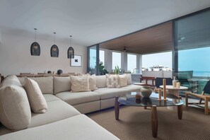 Ein modernes Wohnzimmer mit einer großen Couch, einem Glastisch und Blick auf den Ozean.