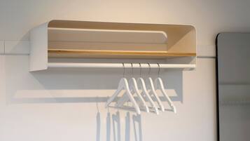 A white wall-mounted shelf with a wooden panel and a white hanging rack with clothes.