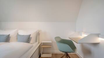 Ein modernes Hotelzimmer mit Bett, Sessel, Nachttisch und Wandlampe.