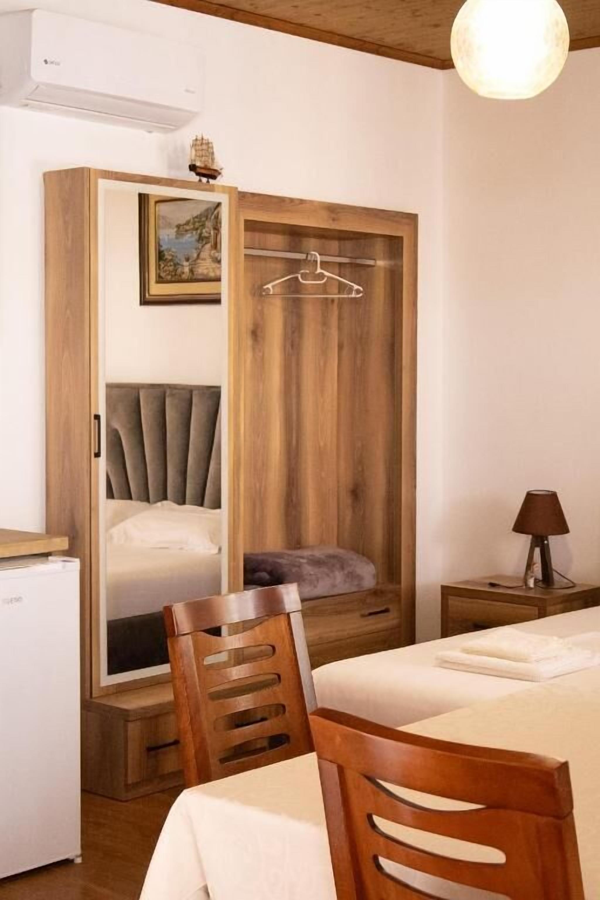 A bedroom with a bed, a wooden wardrobe, a chair, a bedside table, and a lamp.