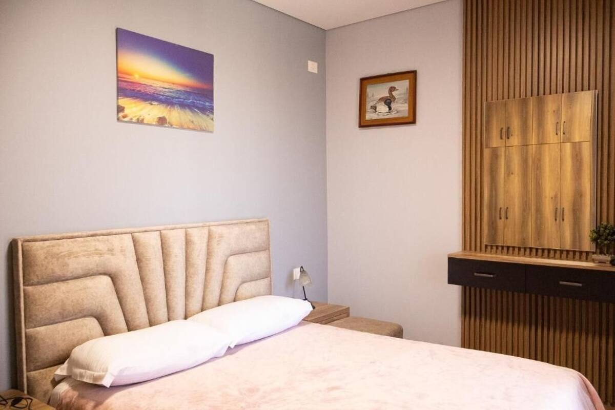 A bedroom with a bed, a wooden wardrobe, a framed picture, and a painting on the wall.