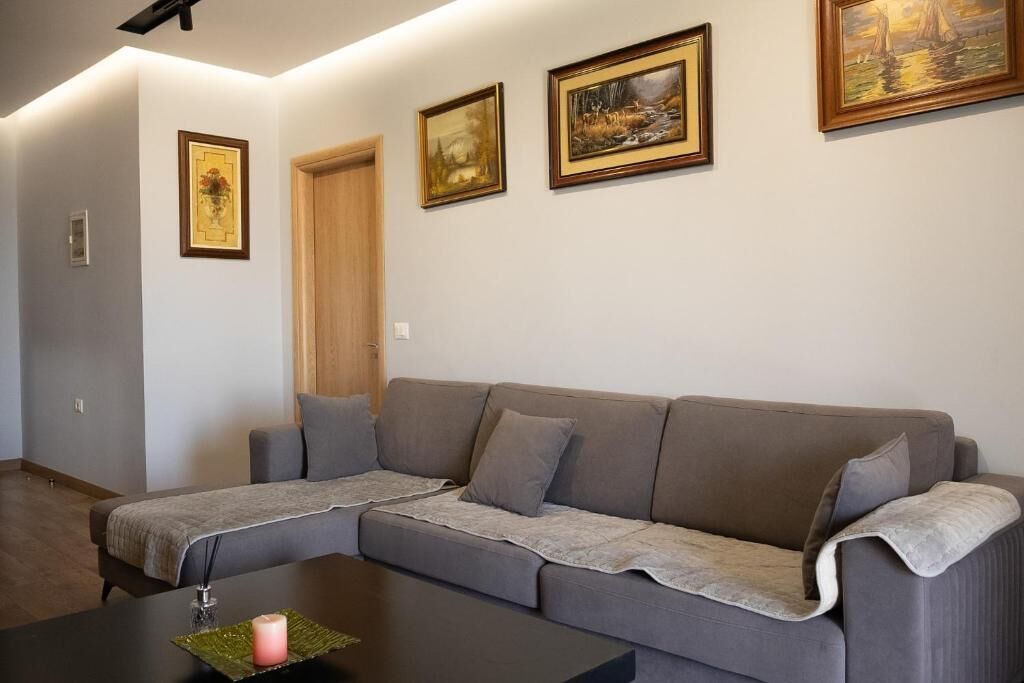 A living room with a grey sofa, a coffee table with a candle, and framed artwork on the wall.