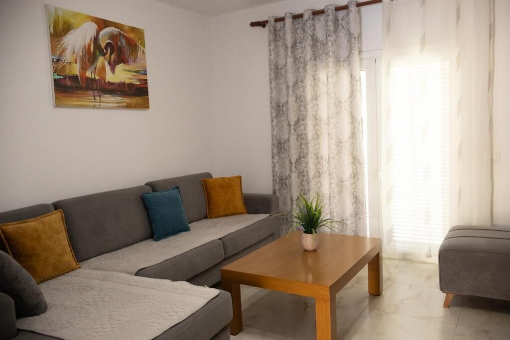 A living room with a sofa, a coffee table, a painting, and a curtain.