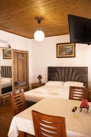 Um quarto com uma cama, uma mesa, cadeiras, uma televisão e um quadro na parede.