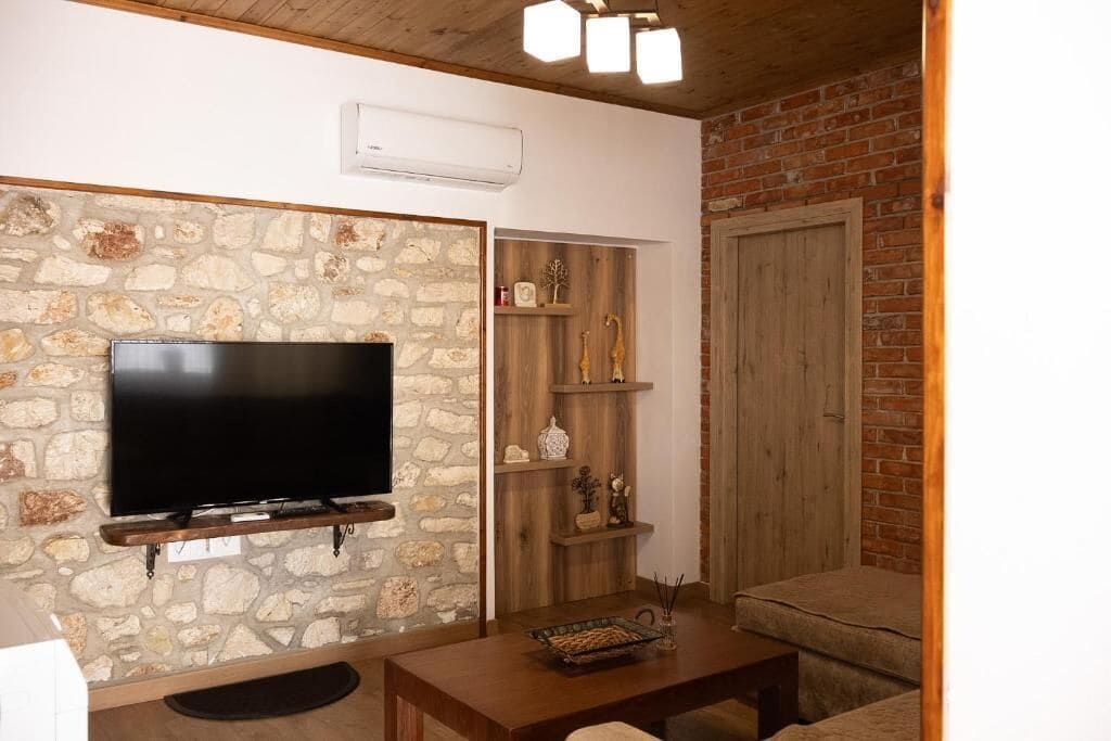 A living room with a stone wall, a mounted TV, wooden shelves, a sofa, and a door.