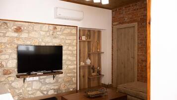 A living room with a stone wall, a mounted TV, wooden shelves, a sofa, and a door.
