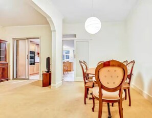 A dining area with a round table and six chairs, a television on a stand, and a hallway leading to a kitchen. - Cosy garden flat in Finchley, North London - Pass the Keys (London)