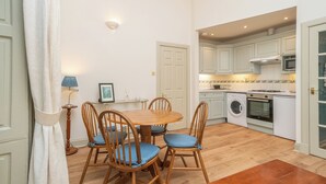 A compact kitchen with a dining area, including a table with chairs, a washing machine, and a microwave. - Charming Georgian flat in the Heart of Edinburgh - Pass the Keys (Edinburgh)