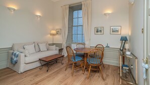 A room with a sofa, a dining table with chairs, a lamp, and a window with curtains. - Charming Georgian flat in the Heart of Edinburgh - Pass the Keys (Edinburgh)