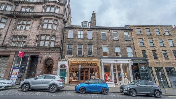 A historic building with a corner entrance, a visible hotel sign, and storefronts with clothing displays. - Charming Georgian flat in the Heart of Edinburgh - Pass the Keys (Edinburgh)