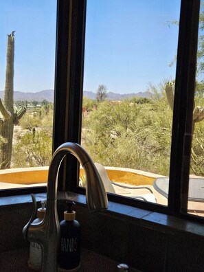 A bathroom with a window view of a desert landscape, a faucet, and a soap dispenser. - Quintessential Tucson 2 -  2BR 2BA Adobe House with Office and VIEWS! (Tucson)