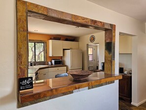A kitchen with a stone backsplash, a microwave, a refrigerator, and a clock on the wall. - Quintessential Tucson 2 -  2BR 2BA Adobe House with Office and VIEWS! (Tucson)