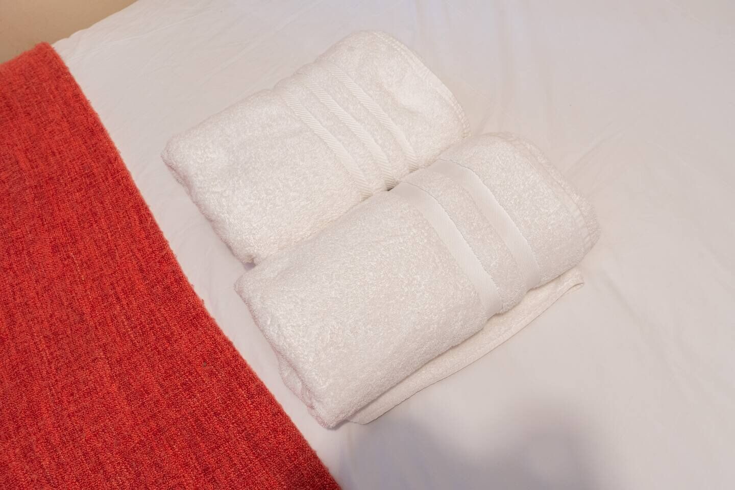 Zwei weiße Handtücher liegen auf einem Bett, ein rotes Handtuch auf der linken Seite.
