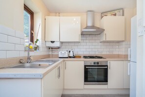A kitchen with white cabinets, a stainless steel sink, a gas stove, and an oven. - Quiet St. Albans Cottage with Free Parking - Pass the Keys (St Albans)