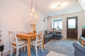 A living room with a wooden dining table, white chairs, a grey sofa, a blue patterned rug, and a lamp. - Quiet St. Albans Cottage with Free Parking - Pass the Keys (St Albans)