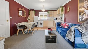 A compact living space with a dining area, kitchen, and a sofa with a Union Jack pillow.