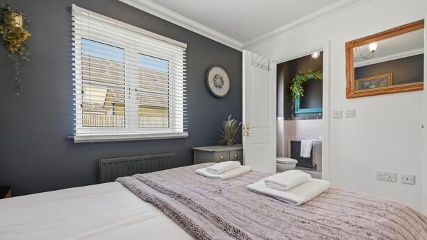 A bedroom with a bed, a window, a radiator, a mirror, and a bathroom visible through an open door.