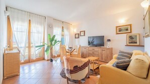 A living room with a sofa, TV, dining table, chairs, and a large plant. - Villa Sorrento - Two Bedroom Apartment, Sleeps 4 (Marina di Massa)