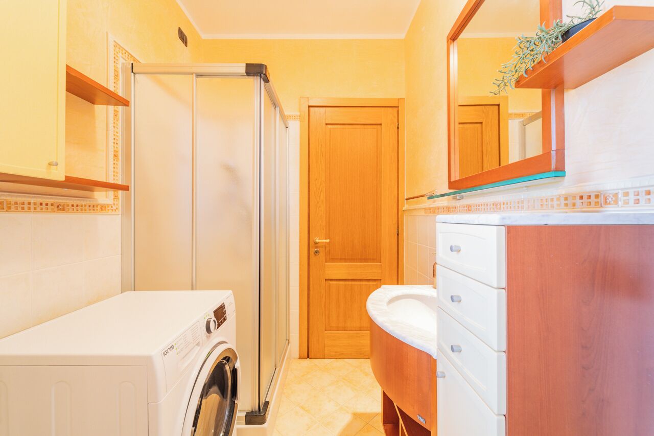A compact bathroom with a washing machine, a wooden door, and a vanity with drawers.