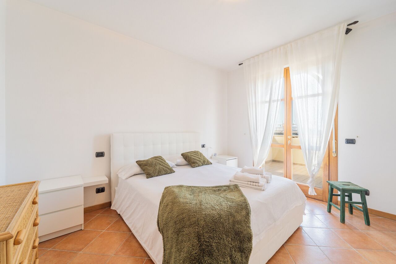 Quarto com cama, mesas de cabeceira, um banquinho e janela com cortinas.