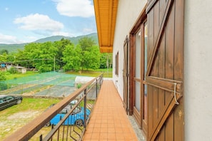 A balcony with a view of a tennis court, a car, and a mountainous landscape.