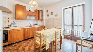A kitchen with wooden cabinets, a dining table with a lemon-patterned tablecloth, and a window with curtains. - All'antico Peso - Two Bedroom Apartment, Sleeps 5 (Festiona)