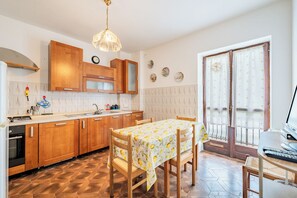 Une cuisine avec des meubles de rangement en bois, une table à manger recouverte d’une nappe à motifs de citron, et une fenêtre avec des rideaux.