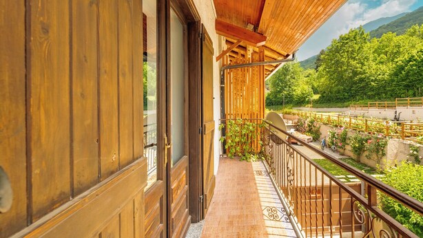 A wooden balcony with a view of a garden and mountains.