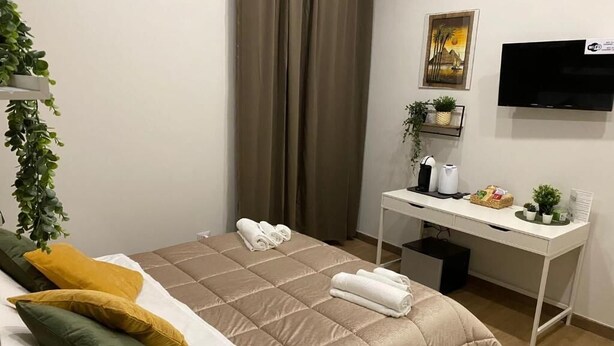 Habitación de hotel con cama, escritorio, televisión y ventana con cortinas.