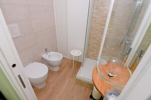Un baño con inodoro, bidé y cabina de ducha con mampara de vidrio.