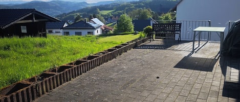 Un chemin pavé mène à un bâtiment à la façade blanche, où se trouvent un banc et une table.