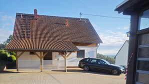 A house with a tiled roof, a covered garage, and a paved driveway. - Vacation apartment on the Nordschleife (Wimbach)