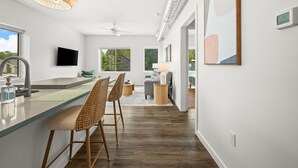 A modern kitchen with a central island, bar stools, a ceiling fan, and a large window.