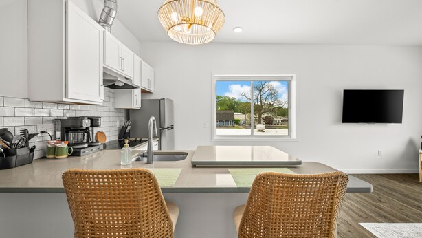 A modern kitchen with white cabinets, a stainless steel refrigerator, a built-in oven, a coffee maker, and a large window offering a view of the outdoors.