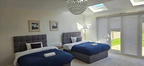 A bedroom with two beds, a chandelier, and a view through large sliding doors. - Large House, Sleeps 7, Perfect for Long term stays (Cottam)
