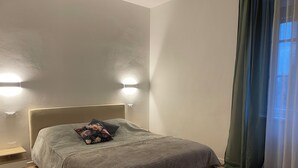 A bedroom with a bed, bedside tables, a wall-mounted light, and a window with curtains. - Cozy Apartment in Verona, Near Station and Old Town (Verona)