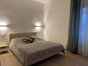 Een slaapkamer met een bed, nachtkastjes, een wandlamp en een raam met gordijnen.