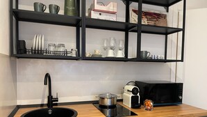 A kitchen with a black sink, a microwave, a toaster, and a shelf with kitchenware. - Cozy Apartment in Verona, Near Station and Old Town (Verona)
