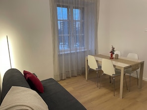 A room with a sofa, a dining table with chairs, a window with sheer curtains, and a lamp. - Cozy Apartment in Verona, Near Station and Old Town (Verona)