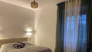 A bedroom with a bed, a wall-mounted light, a window with curtains, and a ceiling light fixture.