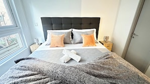 A bed with a tufted headboard, two bedside tables with lamps, a blanket, and pillows. - Moderno depto. en Stgo. cerca del metro (Santiago)