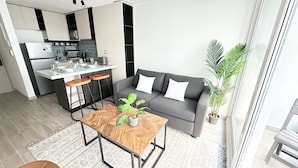 A modern apartment with a kitchen, a grey sofa, a wooden coffee table, and a potted plant. - Moderno depto. en Stgo. cerca del metro (Santiago)