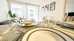 A dining table set with plates, bowls, cutlery, and wine glasses, with a view of the outside through a window. - Moderno depto. en Stgo. cerca del metro (Santiago)