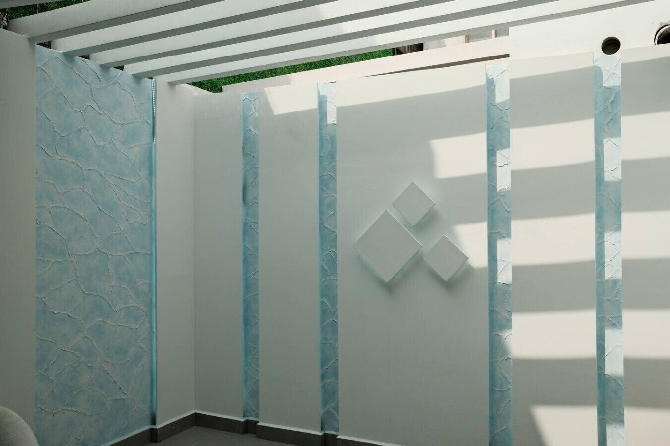 Una stanza con una parete bianca, una parete strutturata a sinistra e un soffitto bianco con travi orizzontali.