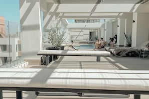A rooftop pool area with sun loungers, a pool table, and a seating area.