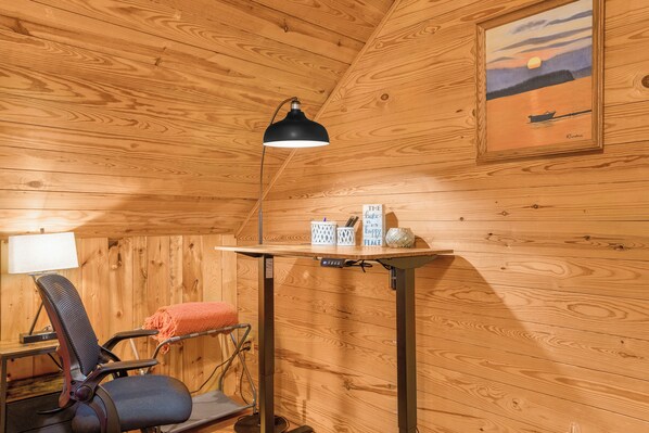 A wooden interior with a desk, chair, lamp, and a painting on the wall.